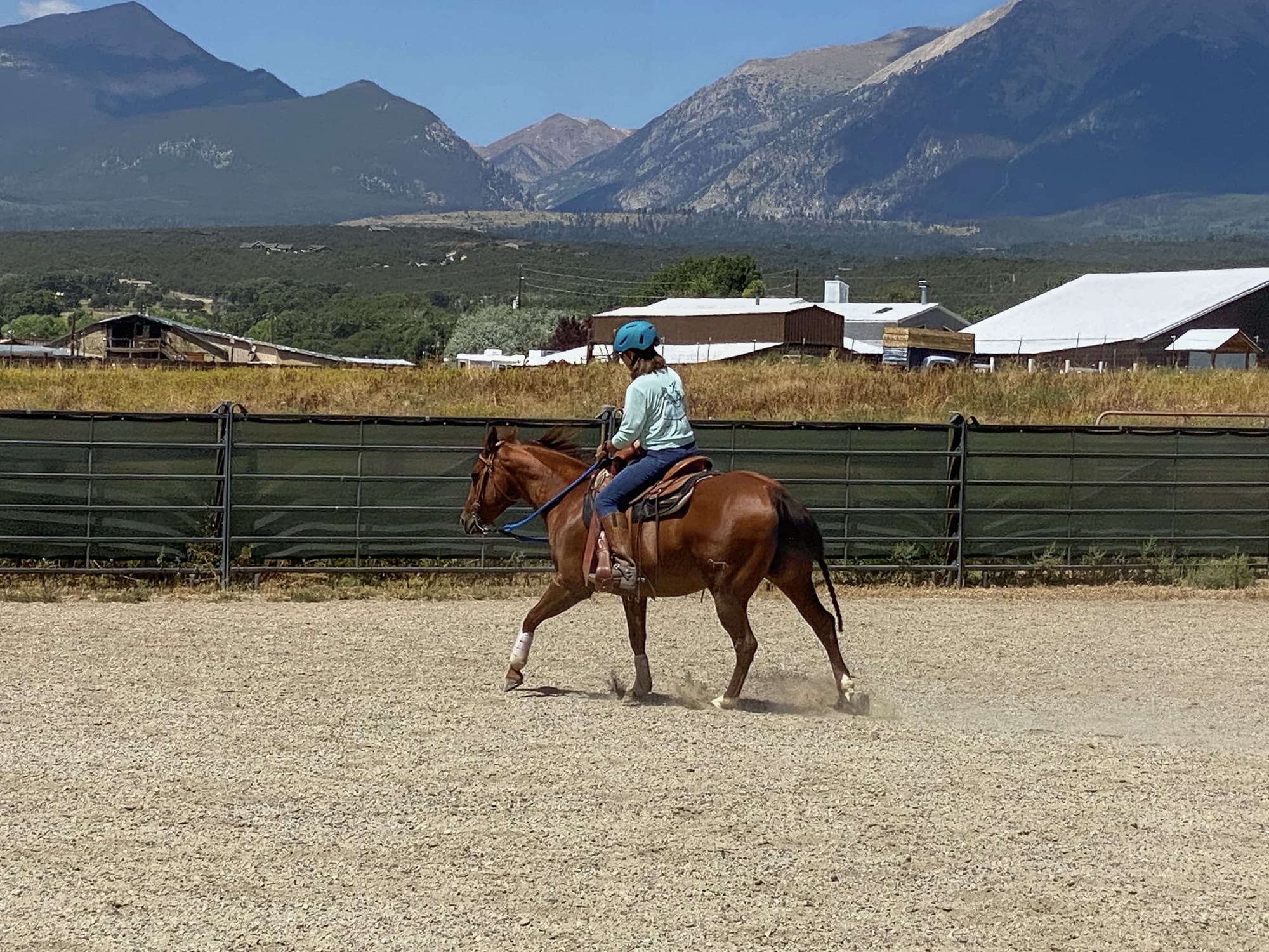 Annie and Juliie cantering in the outdoor arena with mountains in the background.